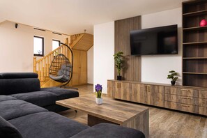 Uma sala de estar moderna com sofá, uma cadeira suspensa, mesa de centro de madeira, TV fixada em uma parede de painéis de madeira e escada que leva a outro cômodo.