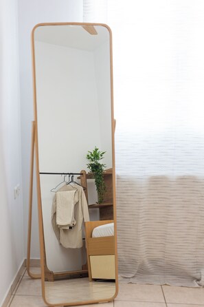 A room with a wooden-framed mirror, a wooden bed, a small plant, and a clothing rack. - Spacious apartment in Naxos Town – 300m from Beach. Ideal for families & friends (naxos town)