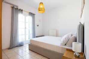 Ein Schlafzimmer mit einem Bett, einem Nachttisch mit Lampe, einem Heizkörper und einem Fenster mit Vorhängen.