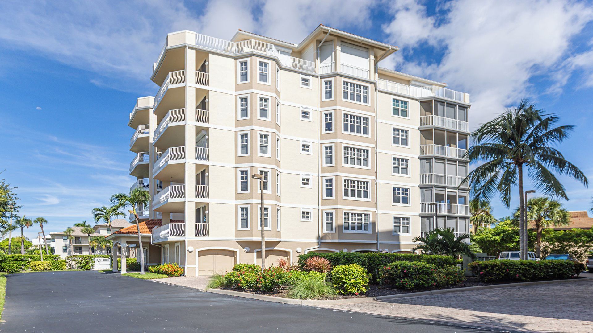 A multi-story hotel with balconies, a parking area, and tropical landscaping.