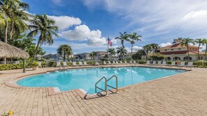 A swimming pool with lounge chairs, palm trees, and a hotel building in the background. - Wake up to island light pouring through the windows of Marco Courtyard Towers (Marco Island)
