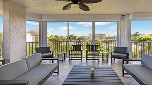 A covered outdoor seating area with a ceiling fan, multiple chairs, a table, and a view of the surrounding buildings and greenery. - 3BR/3BA condo, close to South Beach (Marco Island)