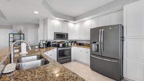 A modern kitchen with white cabinets, stainless steel appliances, granite countertops, and a built-in microwave. - Wake up to island light pouring through the windows of Marco Courtyard Towers (Marco Island)