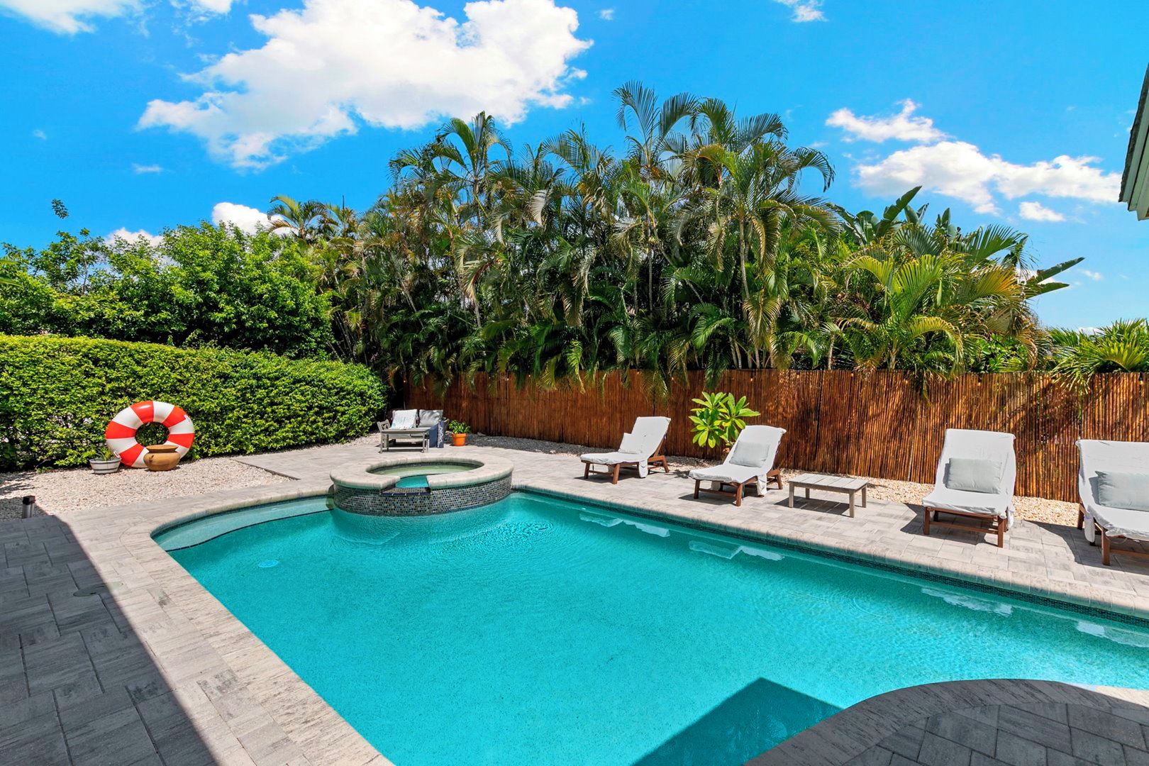 A swimming pool with a wooden deck, surrounded by palm trees and a bamboo fence.
