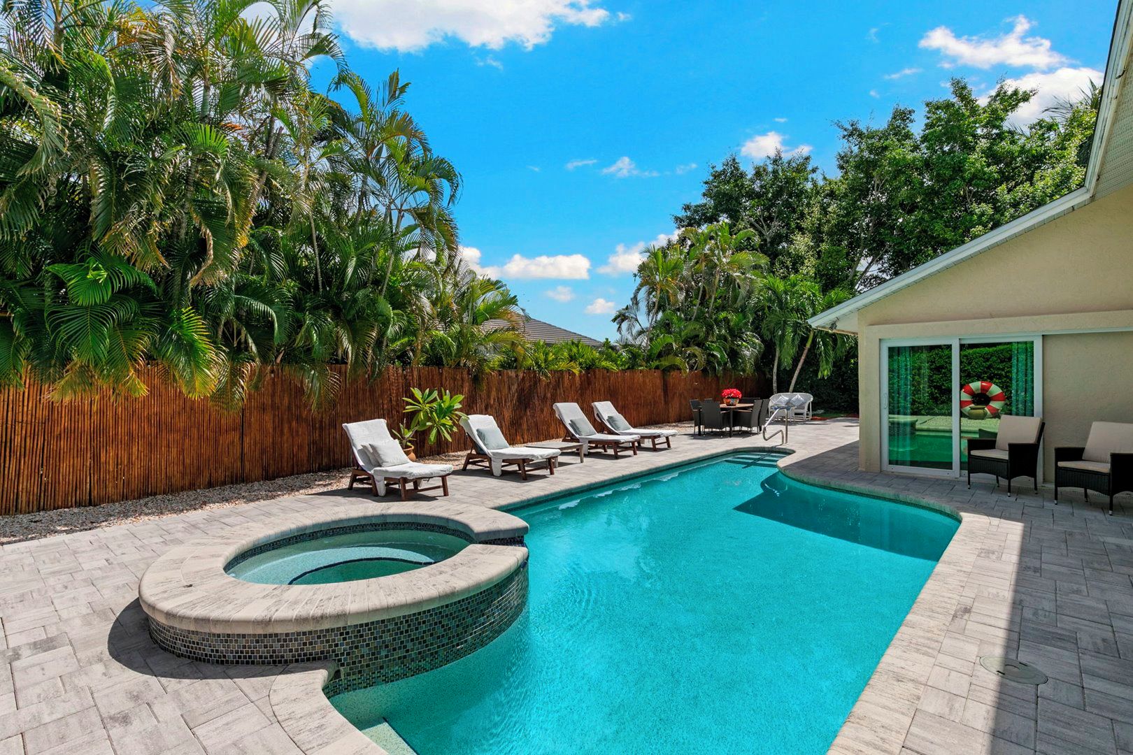 A swimming pool with lounge chairs, surrounded by a wooden fence and tropical vegetation.