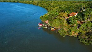 An aerial view of a coastal area with a dock, boats, and a small building with a red roof. - Eco Hotel Leào de Judá - All Inclusive (Curuçá)