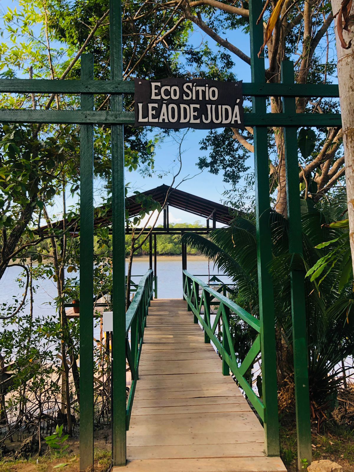 Un puente de madera que lleva a una zona cubierta con un letrero que dice 'Eco Sítio Leao de Juda'.