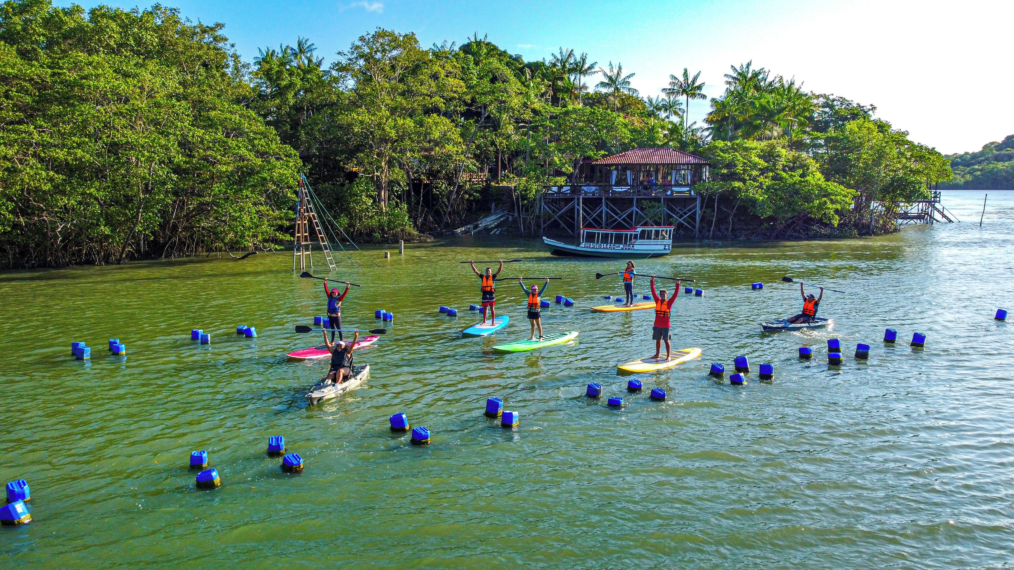 Un grupo de personas haciendo paddleboard en aguas tranquilas, rodeado de abundante vegetación y un barco amarrado.