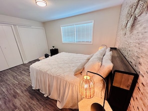 A bedroom with a bed, bedside table, lamp, window, and a wall with a textured pattern.