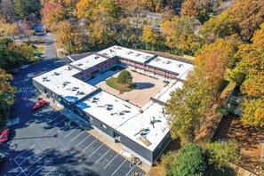 An aerial view of a multi-story building with a flat roof, surrounded by a parking lot and trees with autumn foliage. - NoDa Cottage Near Uptown (Charlotte)