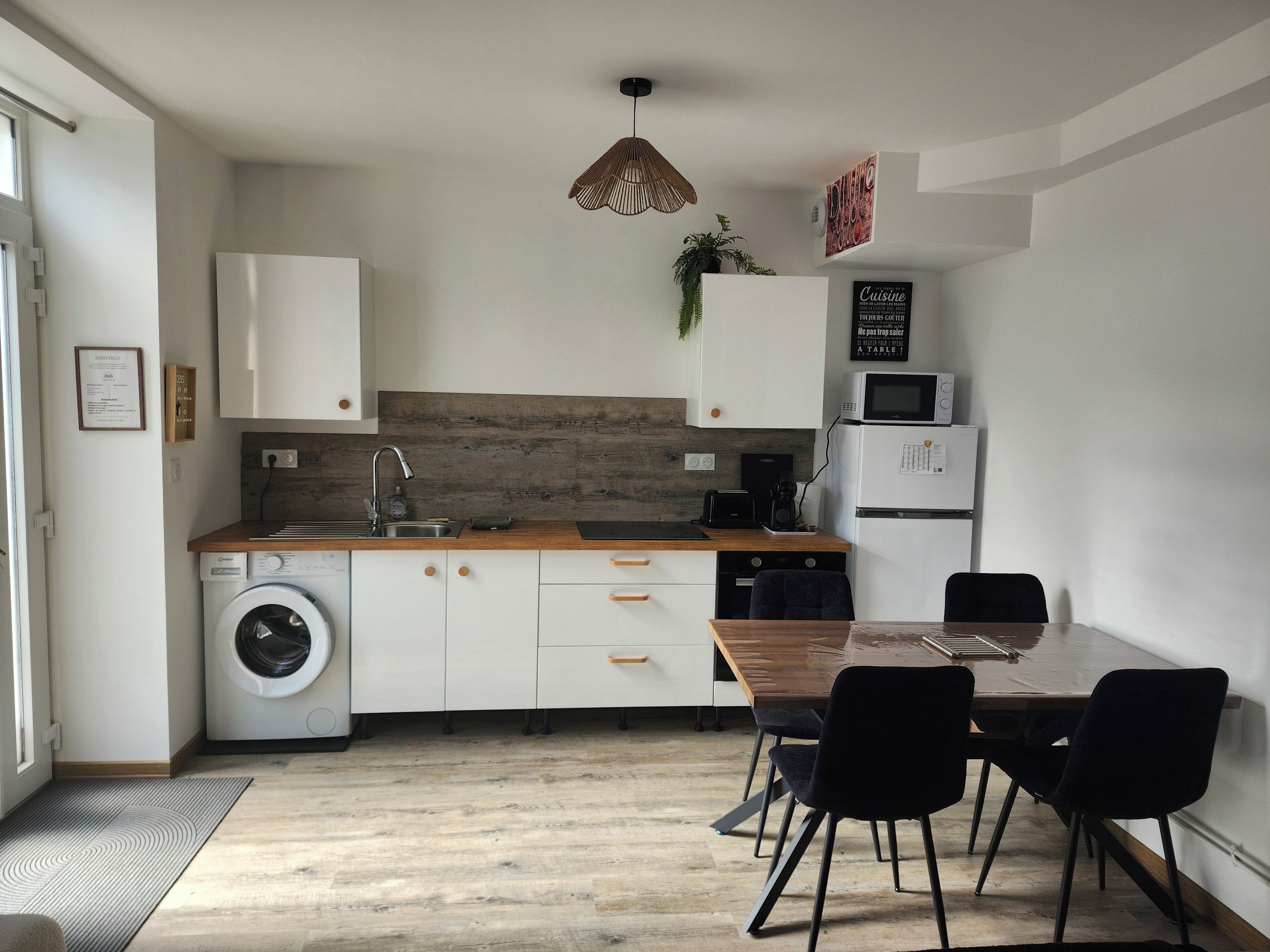 Cocina compacta con lavadora, microondas y zona de comedor con sillas.