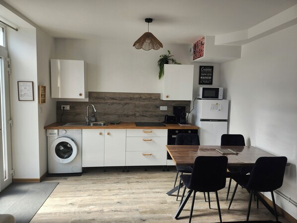 Cocina compacta con lavadora, microondas y zona de comedor con sillas.