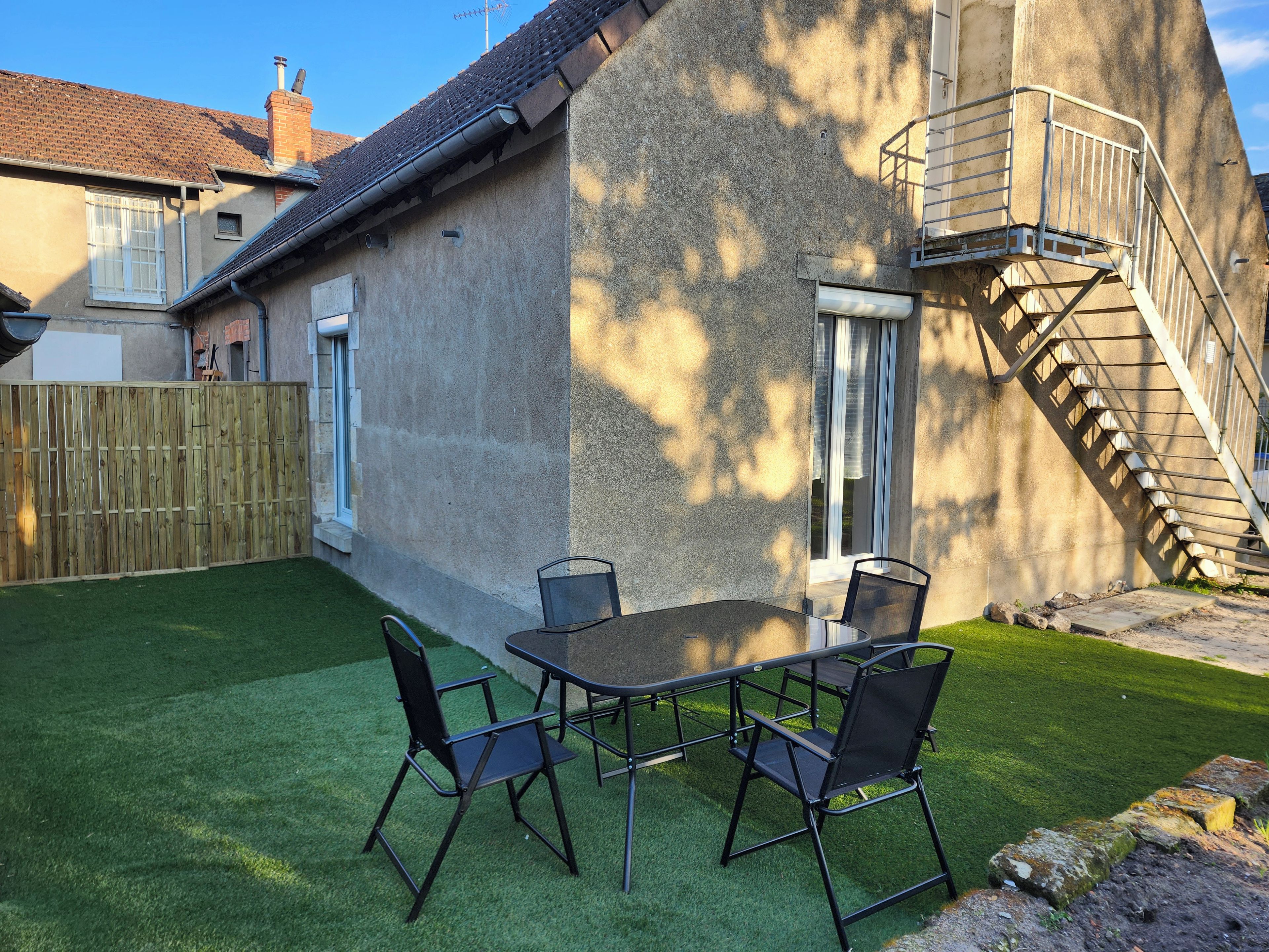 Een terras met een tafel en stoelen, een houten omheining en een betonnen muur met een metalen trap.