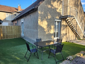 A patio with a table and chairs, a wooden fence, and a concrete wall with a metal staircase.