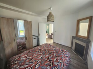 Un dormitorio con cama, espejo, chimenea y puerta que da a otra habitación.