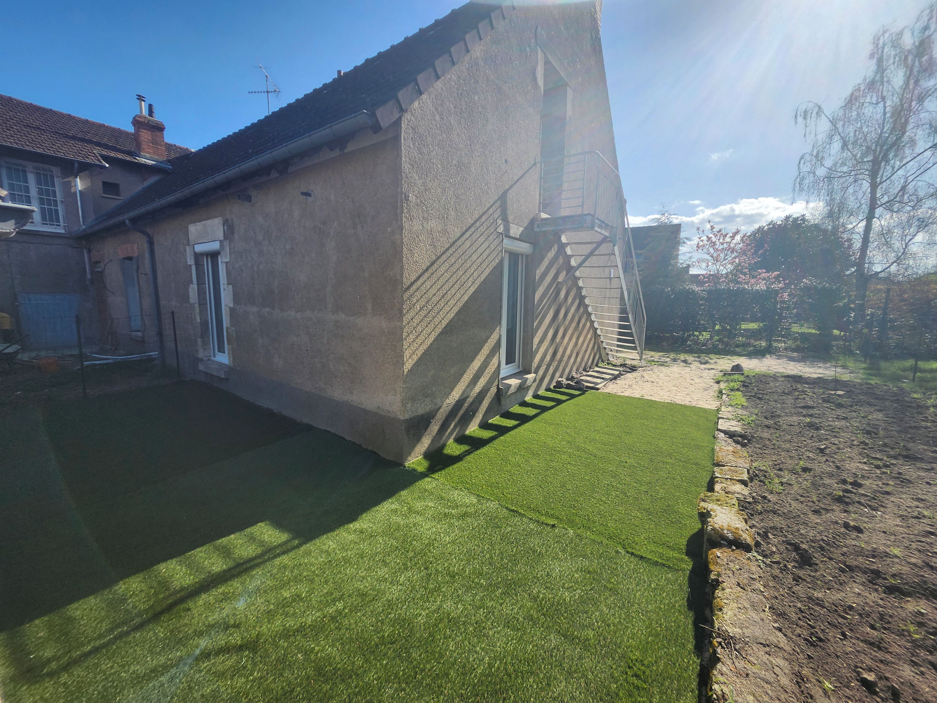 Una propiedad residencial con fachada de concreto, una escalera que lleva a una puerta y un césped bien cuidado.