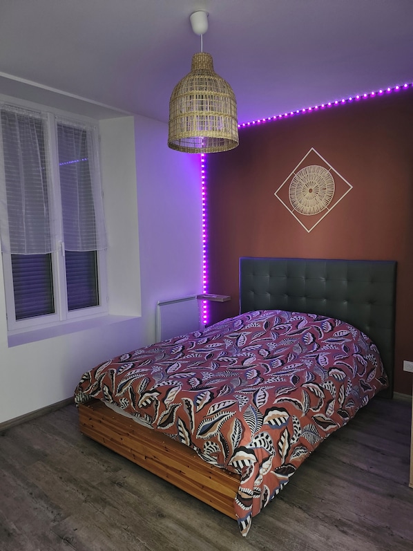 Un dormitorio con cama, lámpara colgante, decoración en la pared y luces LED moradas a lo largo de la pared.