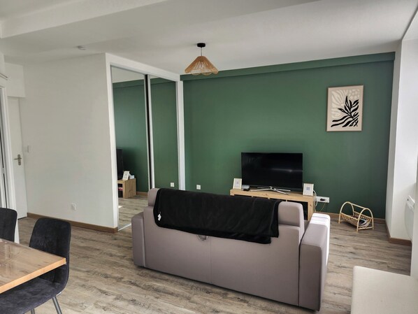 A living room with a grey sofa, a wooden coffee table, a flat-screen TV, and a green accent wall.