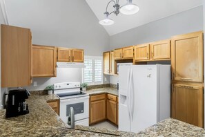 A kitchen with wooden cabinets, a white stove, a refrigerator, and granite countertops. - Cozy apartment only miles from Disney community pool and Jacuzzii (Kissimmee)
