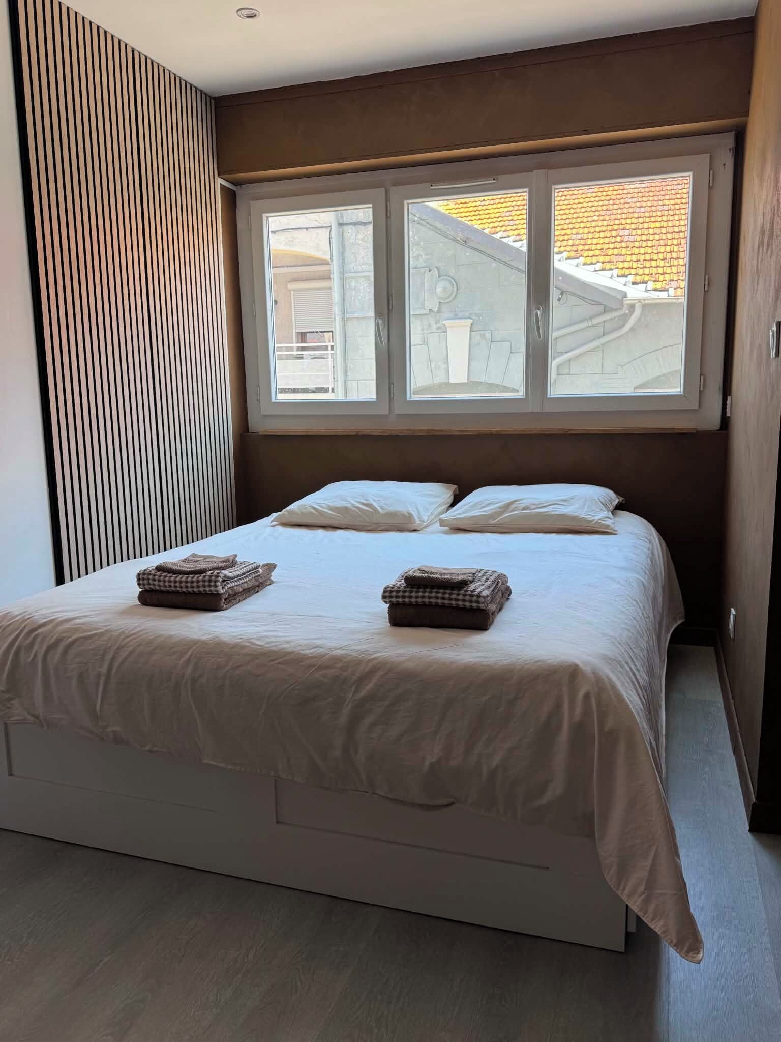 Une chambre à coucher avec un lit, deux fenêtres et une vue sur l’extérieur.