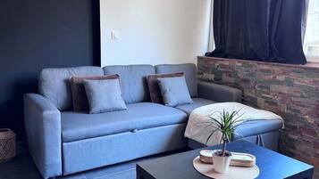 Een moderne woonkamer met een grijze bank, een zwarte salontafel en een potplant.