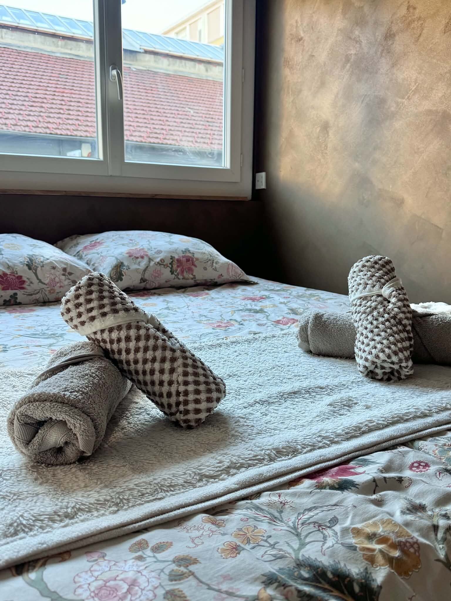 A bed with rolled towels and a floral-patterned bedspread.