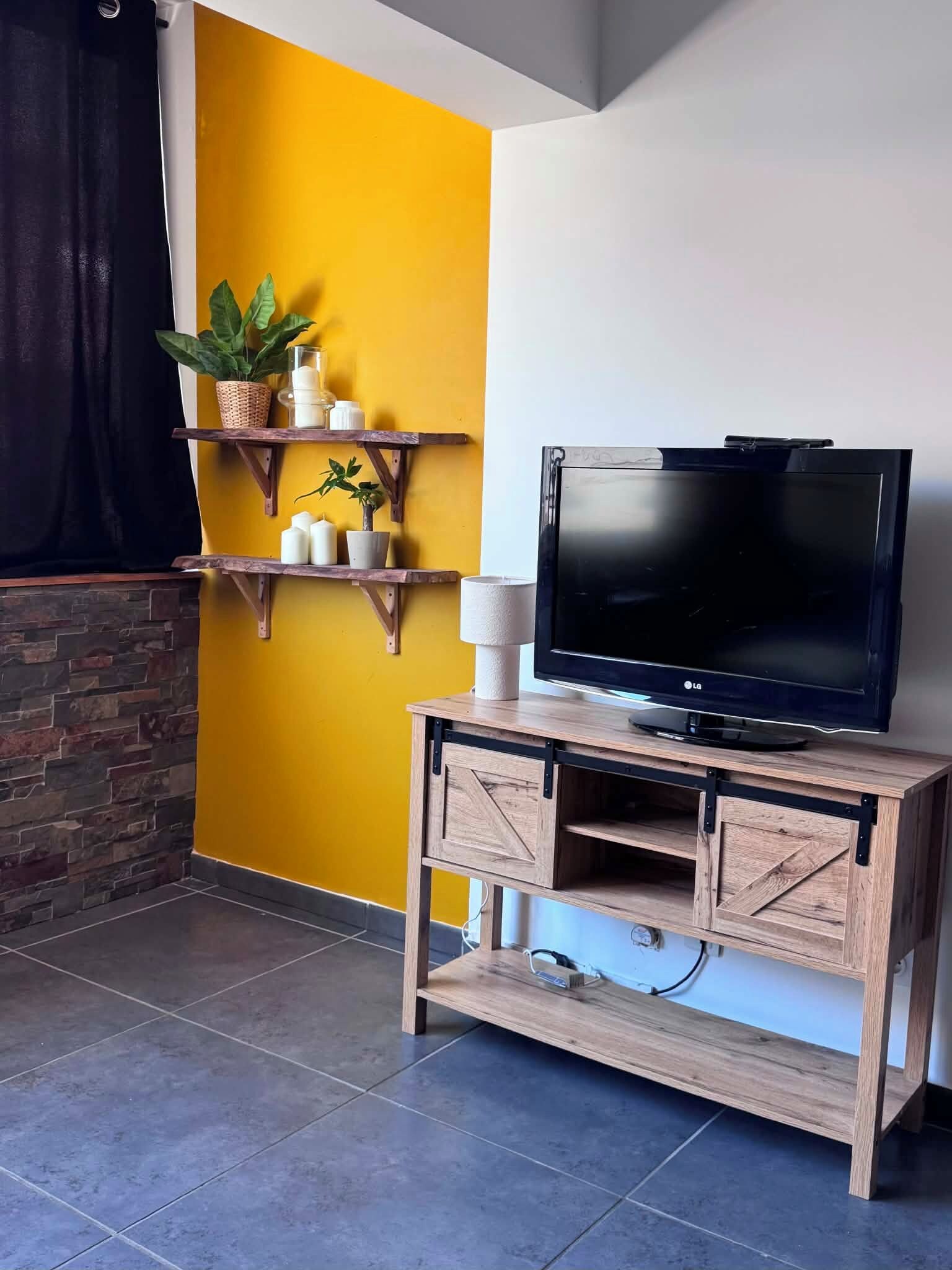 A living room with a TV on a wooden stand, a yellow wall, and a stone wall.
