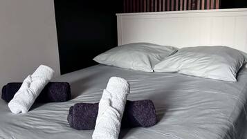 Ein ordentlich bezogenes Bett mit grauen Bettwäsche und zwei zusammengerollten Handtüchern darauf.