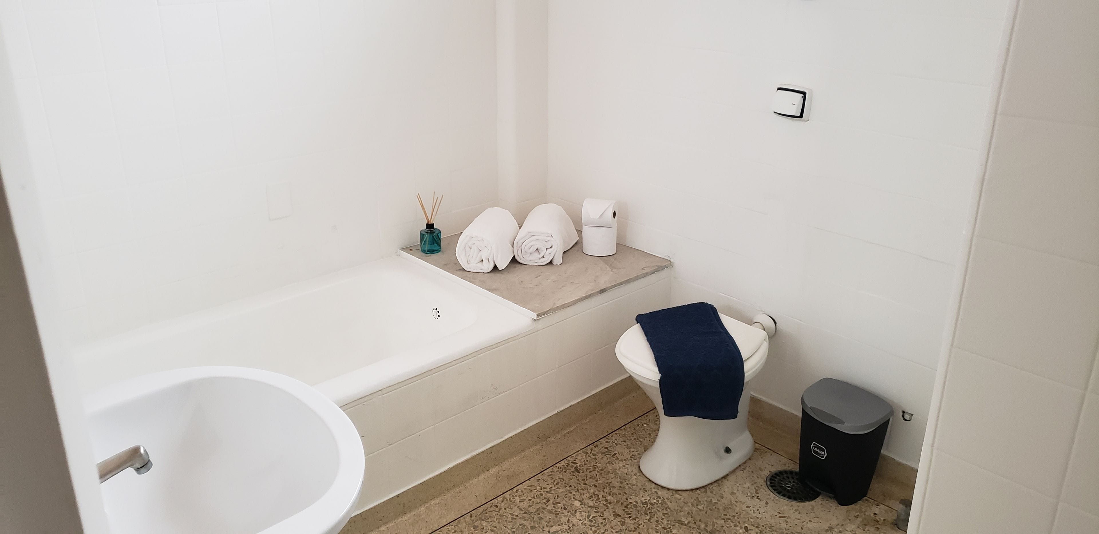 A bathroom with a bathtub, toilet, and a trash bin.