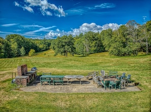 An outdoor seating area with a brick grill and wooden tables and chairs. - Webster Lake Estate 8BR | Beach, Dock, Theater, Gym, Game Room, 700 Acres (Franklin)