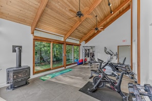 A spacious indoor area with a large sliding glass door leading to a garden, a wood-burning stove, and exercise equipment. - Webster Lake Estate 8BR | Beach, Dock, Theater, Gym, Game Room, 700 Acres (Franklin)