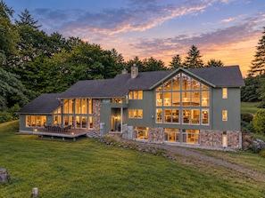 A two-story house with a stone facade, large windows, and a deck. - Webster Lake Estate 8BR | Beach, Dock, Theater, Gym, Game Room, 700 Acres (Franklin)