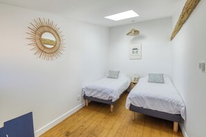 Una habitación con dos camas individuales, un espejo en la pared, una lámpara en el techo y un adorno en la pared.