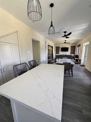 A modern kitchen with a marble island, black chairs, and pendant lighting. - Mullins Retreat — Brand New Architecturally Designed Luxury Villa (Mullins)