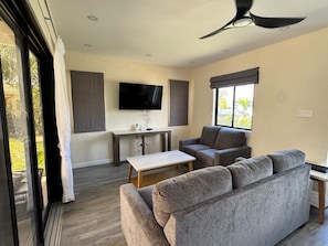 A modern living room with a sofa, a coffee table, a TV mounted on the wall, and a ceiling fan. - Mullins Retreat — Brand New Architecturally Designed Luxury Villa (Mullins)