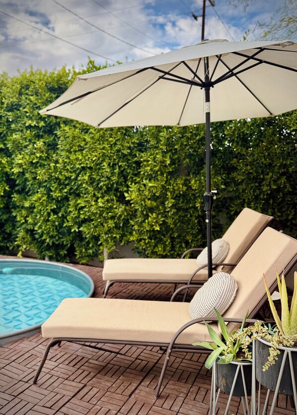 A poolside area with lounge chairs, an umbrella, and potted plants.