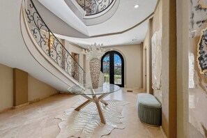 A spacious interior with a glass table, a decorative vase, and a staircase with ornate railings.