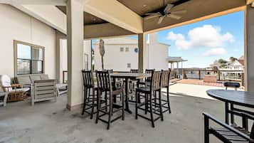 Un patio exterior con mesa y sillas, un ventilador de techo y vista al océano.