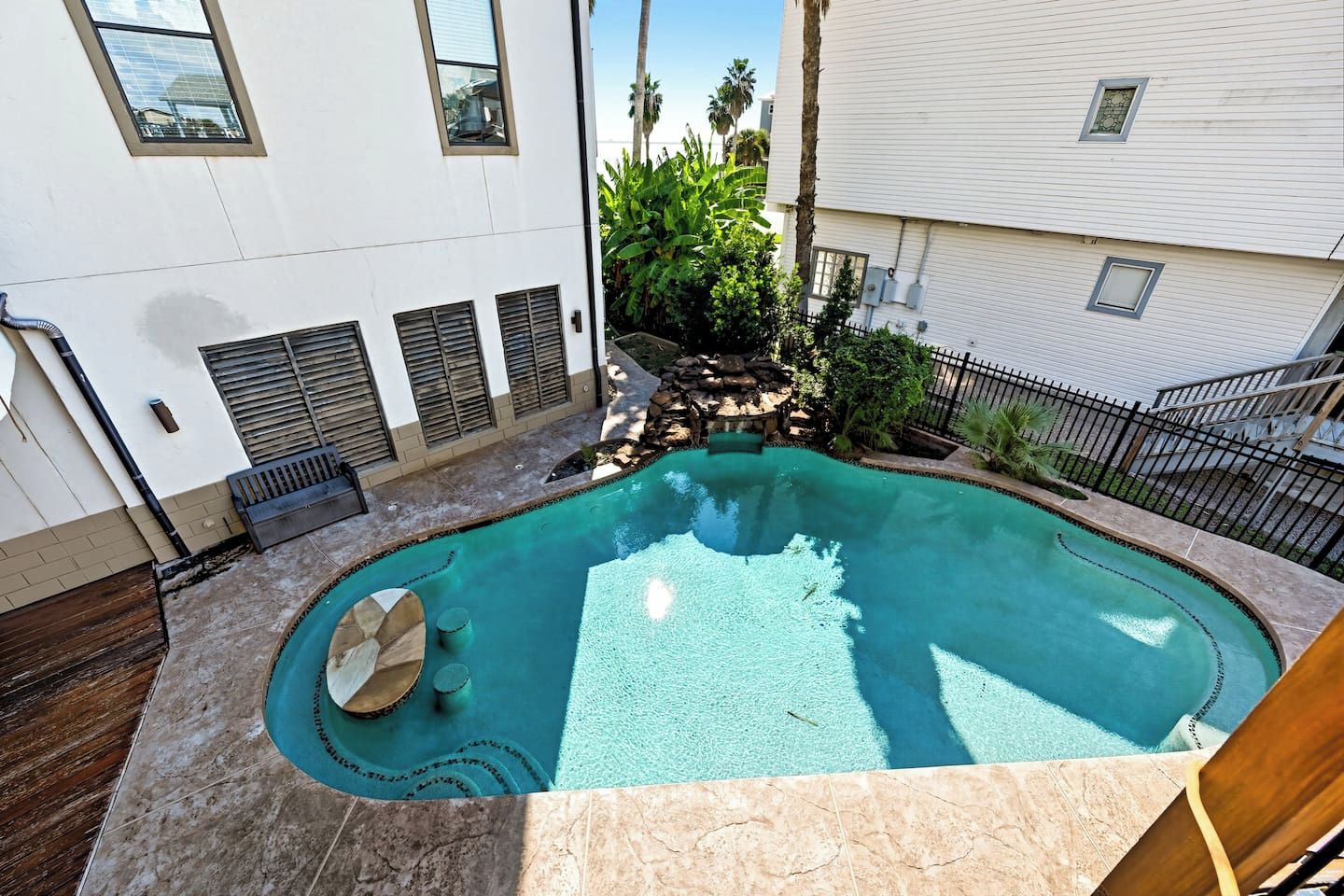 Una piscina con una cascada de piedra, rodeada por un patio con mobiliario y un pequeño jardín.