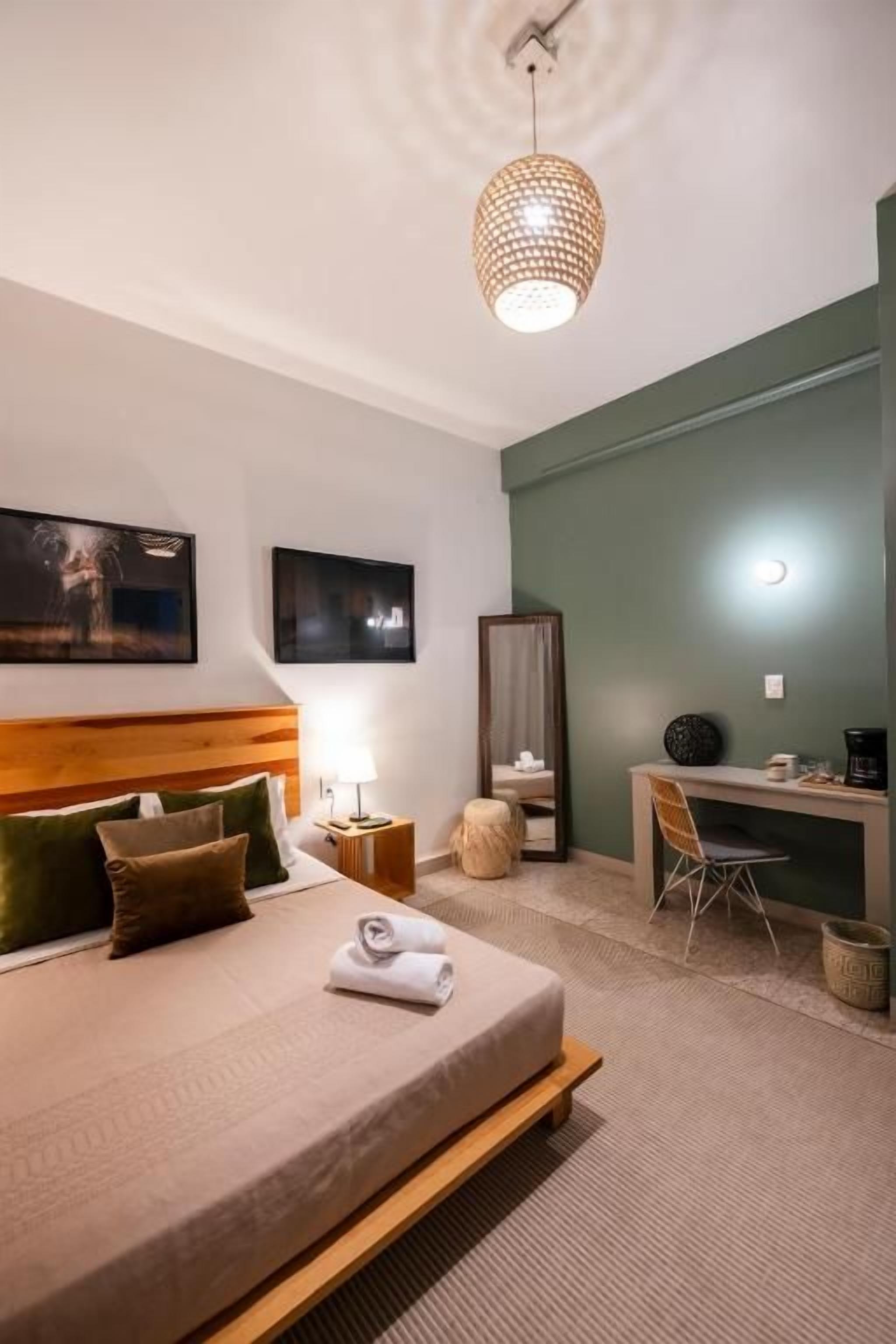 A hotel room with a bed, bedside table, lamp, chair, desk, and a mirror.