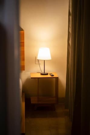 Quarto com mesa de cabeceira, luminária e controle remoto.
