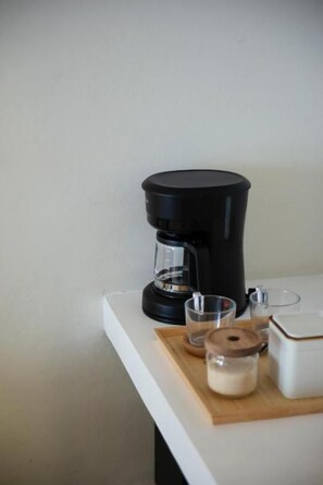 Máquina de café sobre bancada branca, com um copo, um pote e um recipiente.