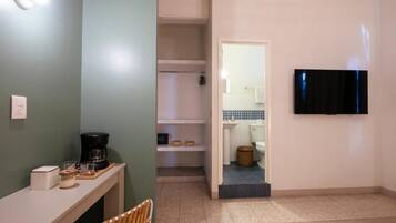 A room with a bed, a bedside table with a lamp, a chair, and a television mounted on the wall.