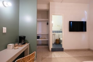 Una habitación con cama, mesita de noche con lámpara, silla y televisión montada en la pared.