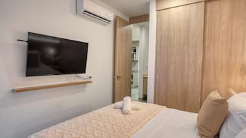 Un dormitorio con una cama, un televisor instalado en la pared, un armario de madera y un equipo de aire acondicionado.