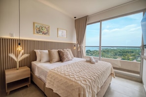 Un dormitorio moderno con una cama grande, una mesita de noche, un jarrón con plumas de pampa, dos cuadros en la pared y un amplio ventanal con vistas a la ciudad.