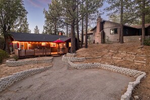 A cabin with a gravel driveway, wooden deck, and a red umbrella. - The Village Villa - Hot Tub, Walk to village (Big Bear Lake)