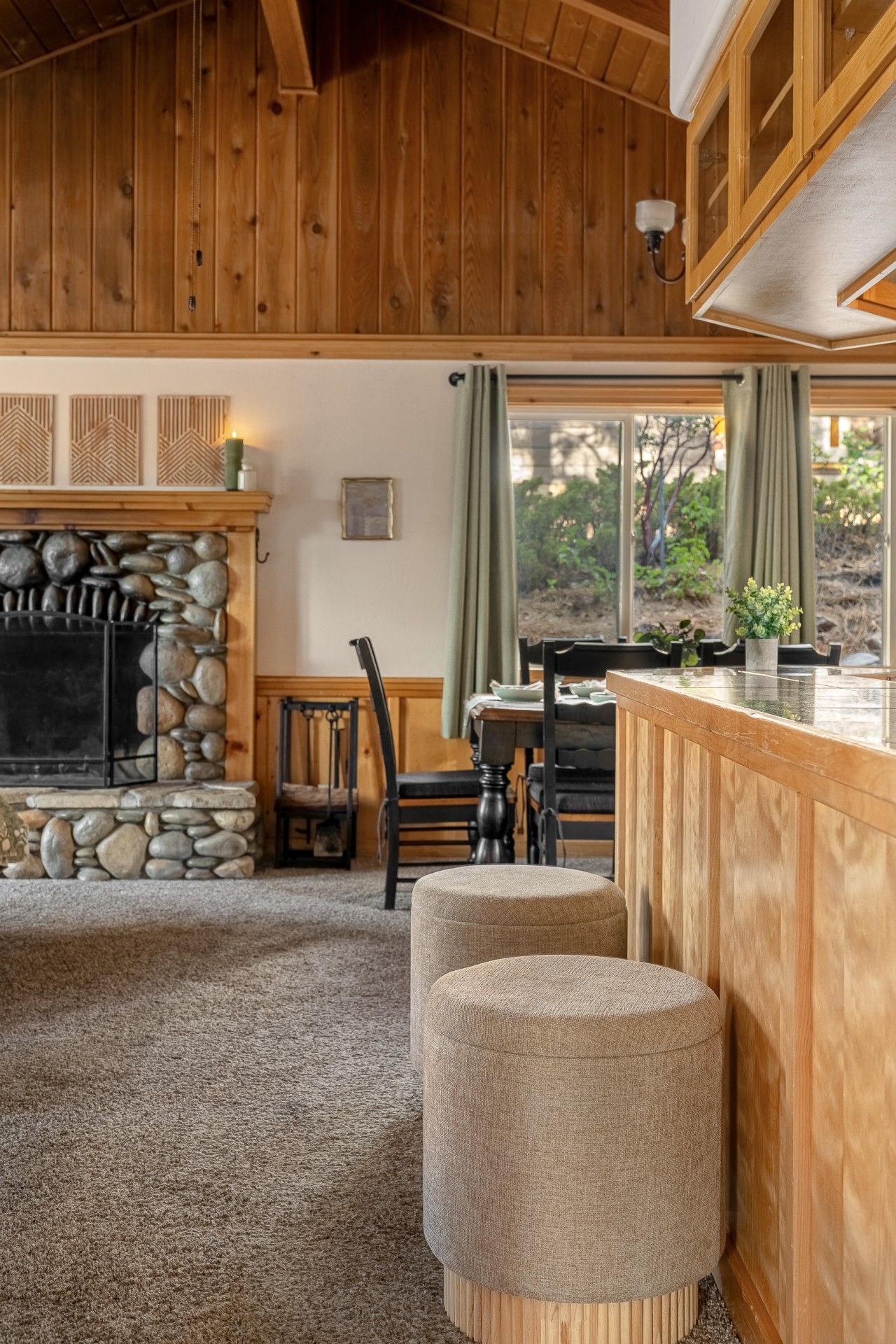 Un intérieur de chalet chaleureux avec une cheminée en pierre, des murs en bois, un coin repas et un bar.