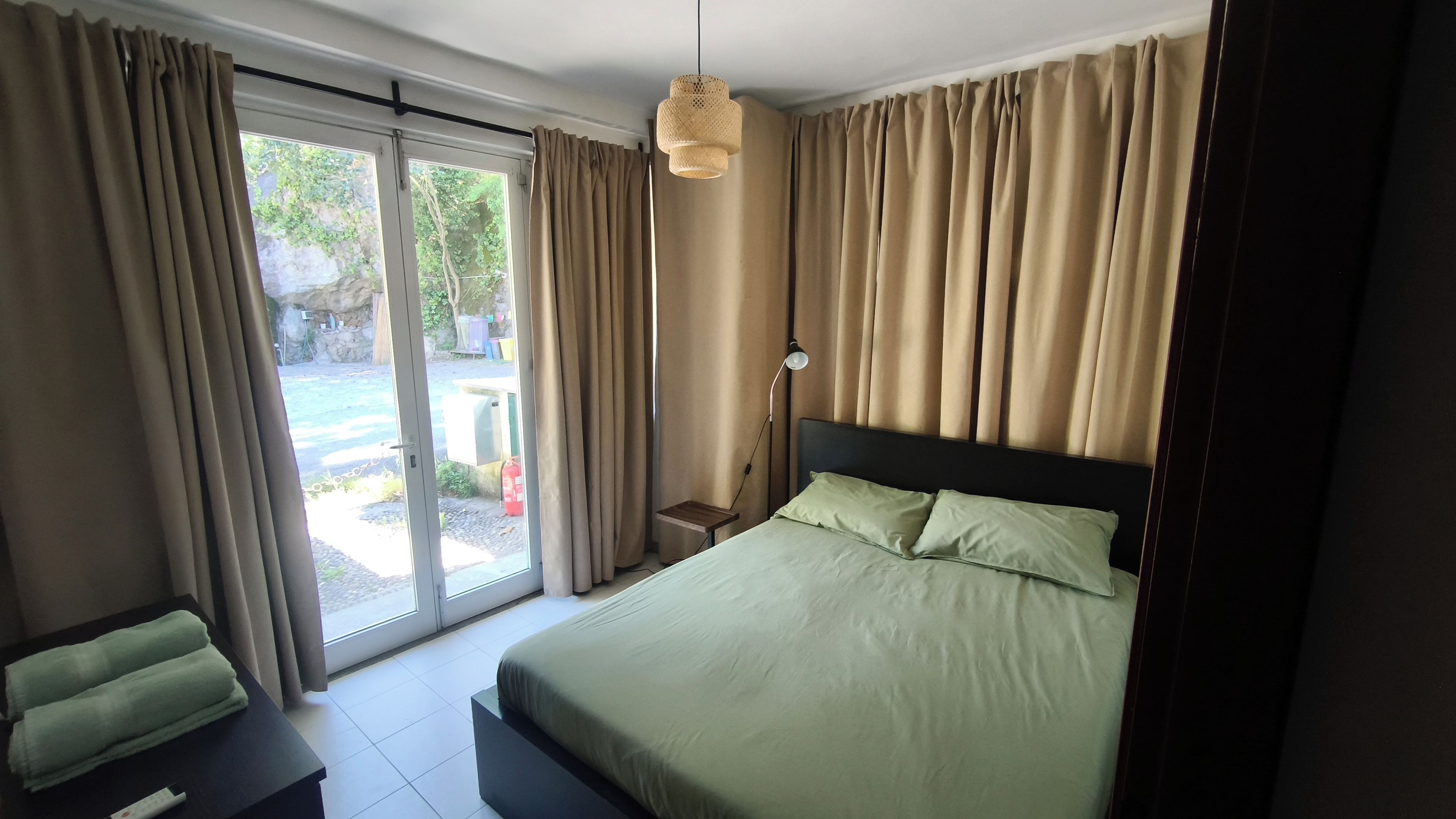 A bedroom with a bed, a nightstand, a lamp, and a view through a sliding glass door to an outdoor area.