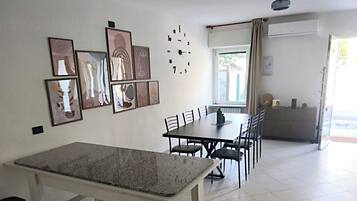 Ein geräumiges Zimmer mit Esstisch, Stühlen, einer Uhr und gerahmten Kunstwerken an der Wand.
